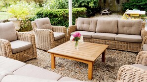 A wicker sofa set with cushions, a wooden coffee table, and a vase with flowers.