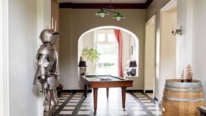 A hallway with a checkered floor, a pool table, a potted plant, and a wooden barrel.
