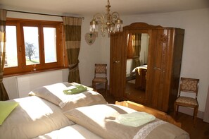 Een slaapkamer met een bed, een houten garderobe, een spiegel en een raam met gordijnen.