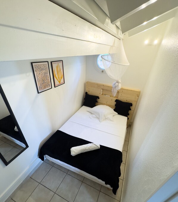 Een kleine, compacte kamer met een stapelbed, klamboe en lijstwerken aan de muur.
