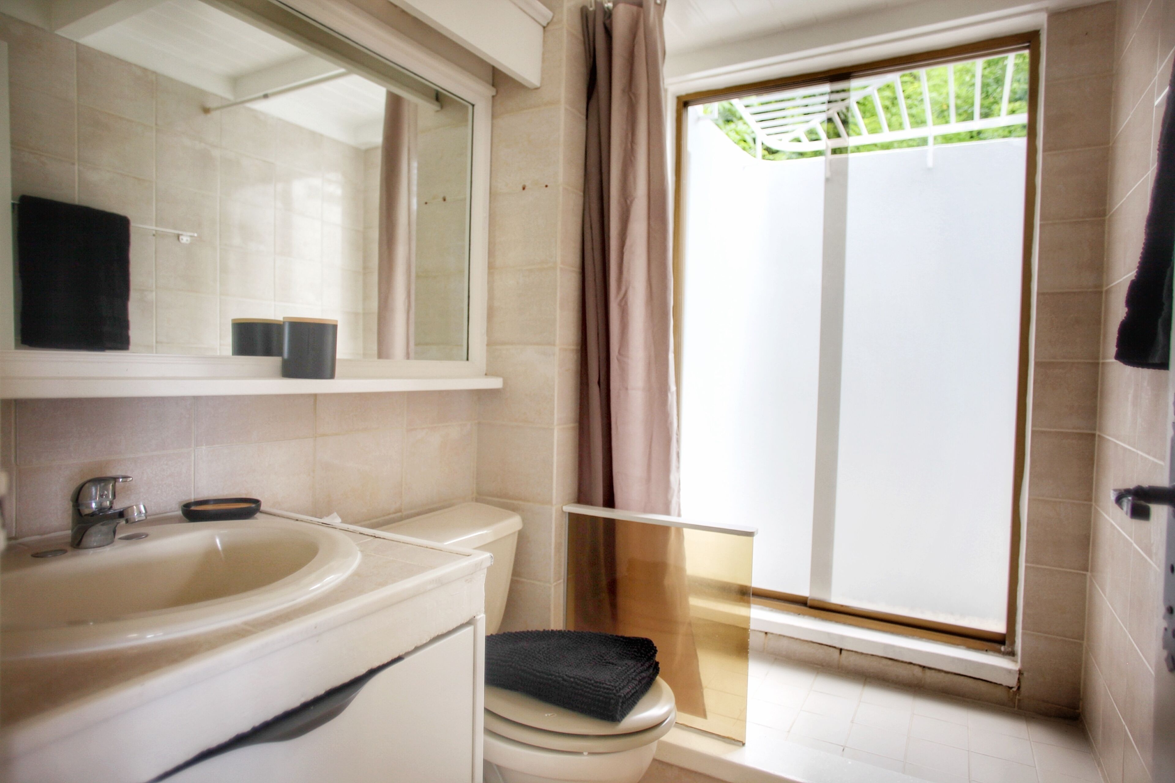 Un baño con lavamanos, inodoro y ventana que da a un espacio exterior cubierto.