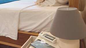 Un dormitori amb un llit, una làmpada de nit, un telèfon i una finestra que donen a vistes de vegetació.