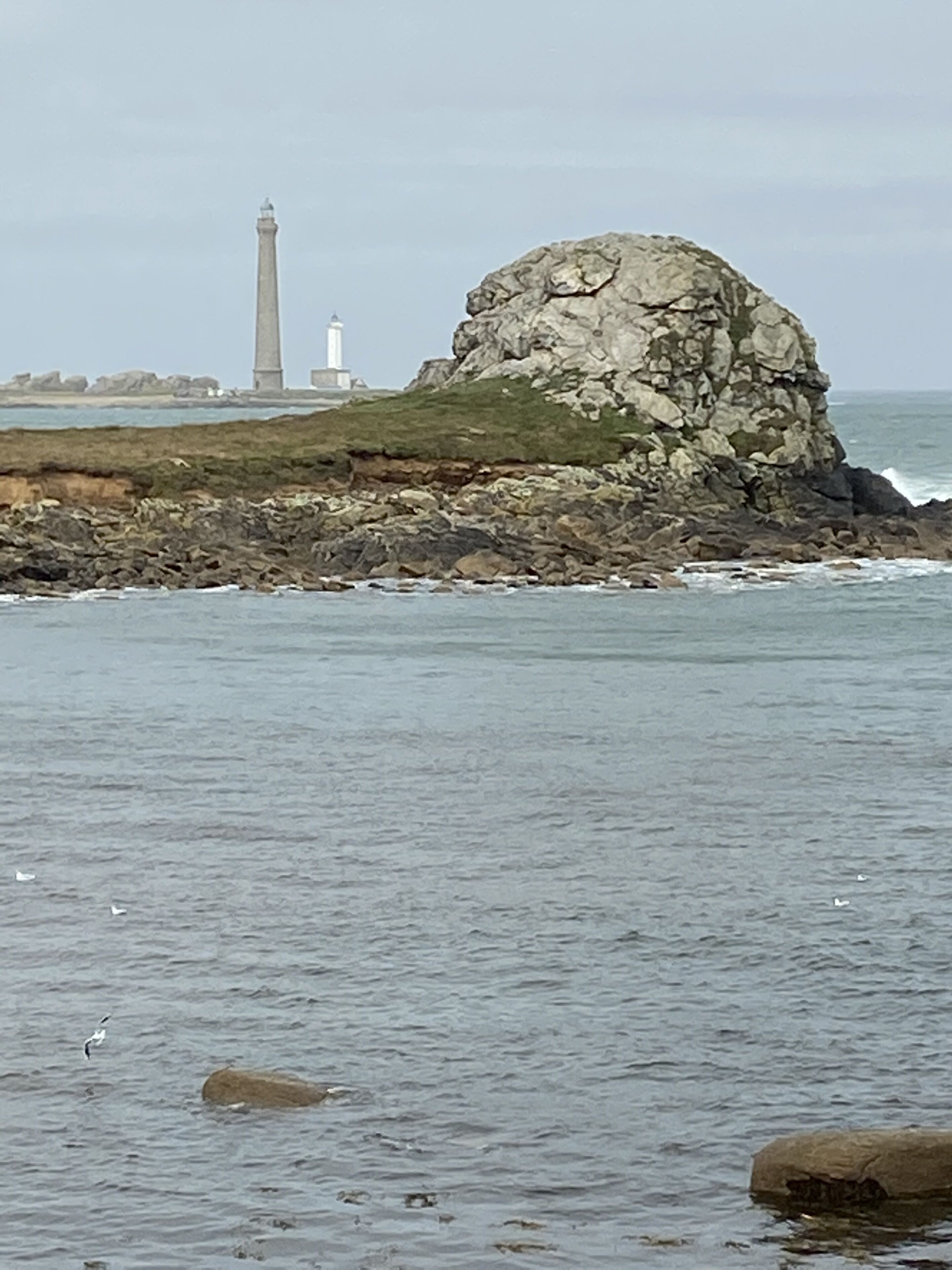 Eine felsige Küstenlinie mit einem Leuchtturm im Hintergrund.