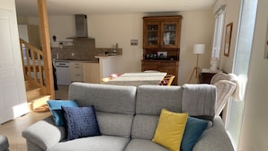 Una sala de estar con un sofá gris, una mesa de comedor y una cocina al fondo.