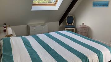 Une chambre avec un puits de lumière, un lit avec une literie à rayures, une commode, une chaise et une lampe fixée au mur.