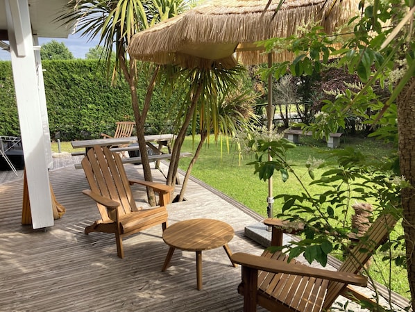 A wooden deck with outdoor furniture, a thatched umbrella, and lush greenery.