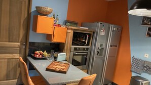 A compact kitchen with a microwave, oven, and refrigerator. There is a wooden door, a table with chairs, and a fruit bowl on the counter. - Family villa for 7 people in a quiet location NEAR THE LAKE AND THE OCEAN, with a terrace and a pool table   (Gironde)