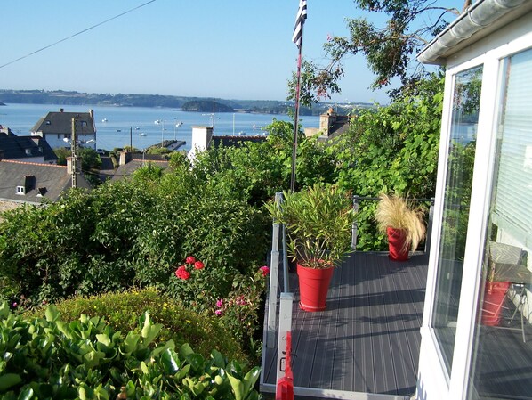 A balcony with potted plants, a view of the sea, and a flag.