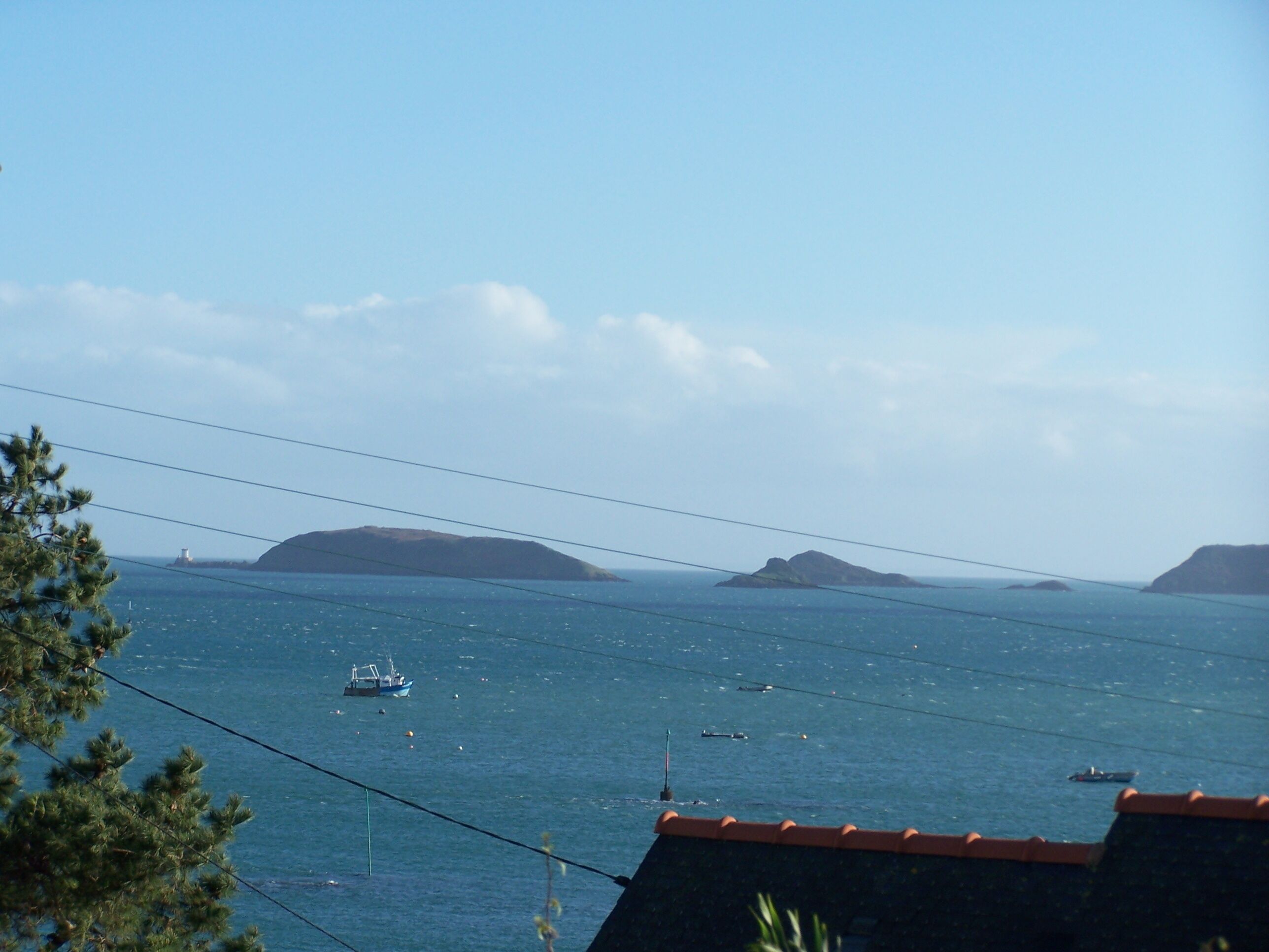Une vue sur la côte, avec un ciel dégagé, un phare et plusieurs bateaux sur l’eau.