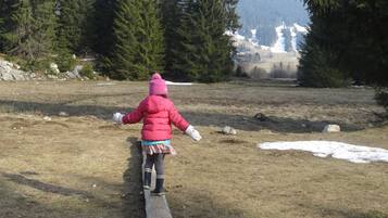 Ein Kind geht auf einer Holzbrücke in einem bewaldeten Gebiet mit Schneeflecken und Bäumen.