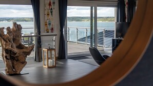 Ein modernes Wohnzimmer mit einer großen Holzskulptur, einem Glastisch und Seeblick durch große Fenster.