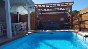 A swimming pool with a wooden deck and chairs, a covered seating area, and a hot tub. - THE FLAMBOYING VILLA at the estate "LES LODGES DE MALENDURE" (Bouillante)