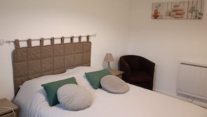Et soveværelse med seng, puder, et natbord, en lampe, en stol og en radiator.