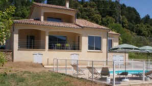 A two-story house with a swimming pool, outdoor seating, and a view of the surrounding hills. - Renting a villa with private pool in the country. (Les Salelles)
