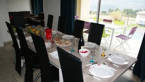 A dining table set for six with chairs, plates, glasses, and a bottle of wine. - Renting a villa with private pool in the country. (Les Salelles)