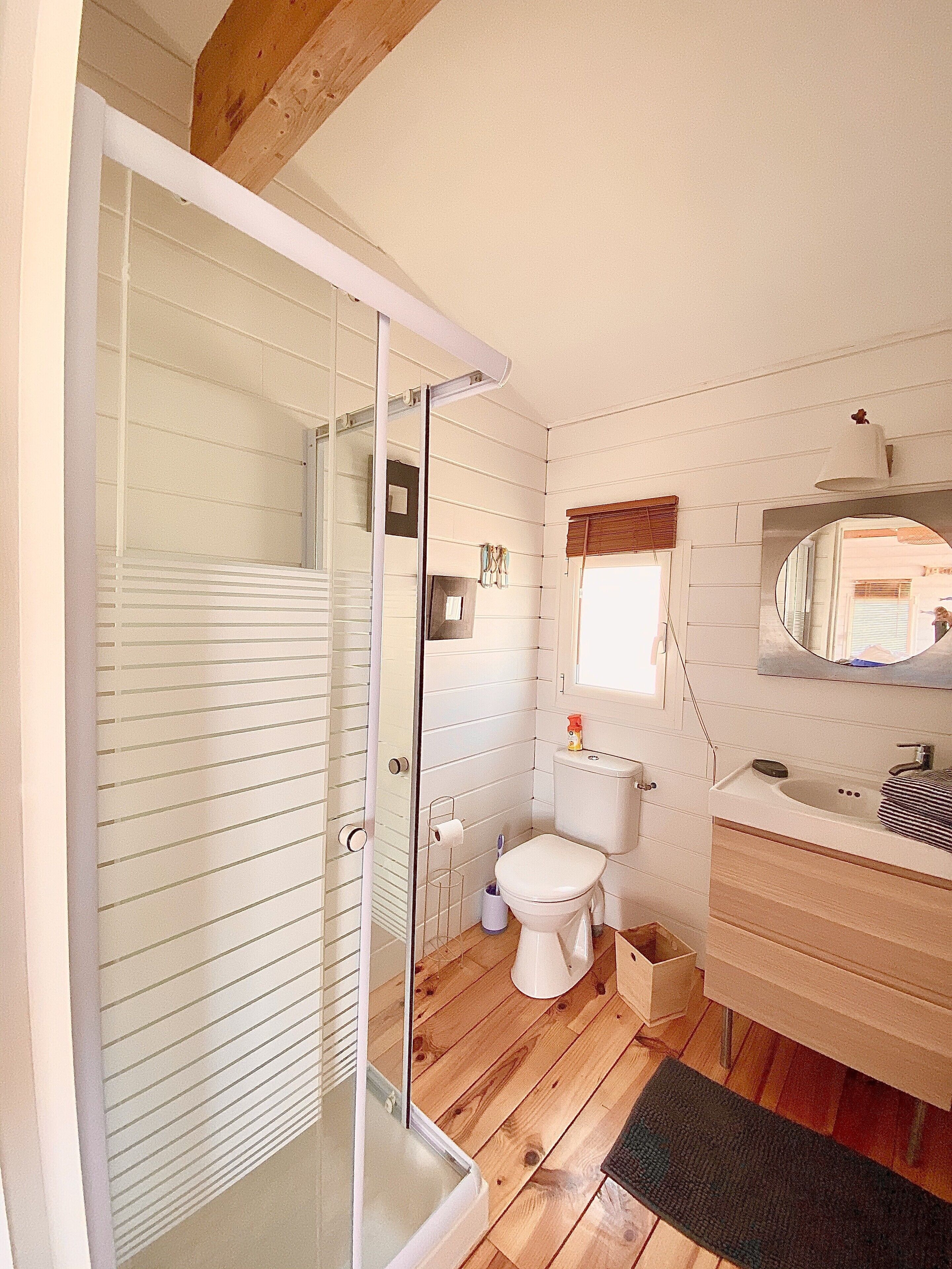 Une salle de bain avec une porte de douche en verre, des toilettes, un lavabo avec un miroir et un revêtement de sol en bois.