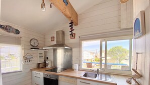 Una cocina compacta con armarios blancos, una campana extractora de acero inoxidable, lavavajillas y una ventana con vista al vecindario.