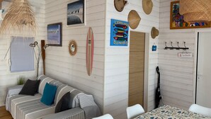 Una habitación con un sofá a rayas, una tabla de surf, un reloj y una pared con varios adornos, incluyendo un cartel de peces y un sombrero.
