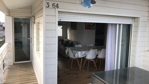 Un espacio al aire libre techado con una mesa y sillas, una entrada con puerta de vidrio y el número '364' en la pared.