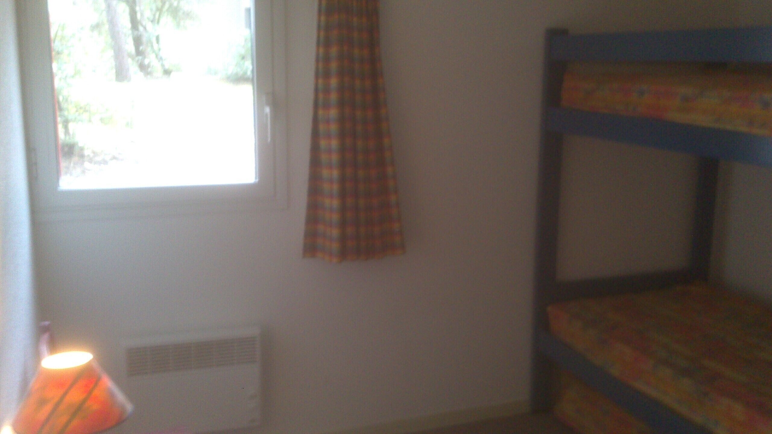 Una habitación con literas, una ventana con cortina y un radiador.