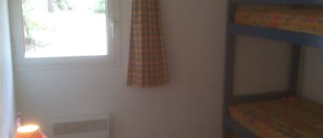 Una habitación con literas, una ventana con cortina y un radiador.