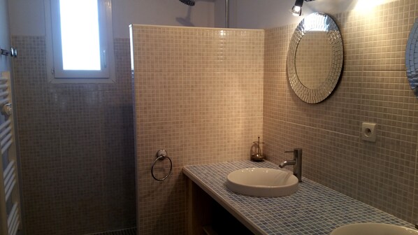 A bathroom with a tiled shower, a sink, and a mirror.