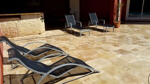 A patio area with tiled flooring, a stone wall, and metal-framed lounge chairs.
