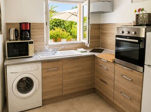 A compact kitchen with a washing machine, a coffee maker, and a stove. - Le Marronnier Vacation Rental – Accessible to People with Disabilities – Mont Ventoux & Cycling (Monieux)
