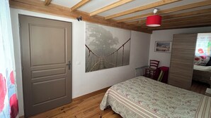 Ein Schlafzimmer mit Holzbalkendecke, einem Bett mit floralem Überwurf, einem Gemälde einer Brücke und einer roten Lampe.