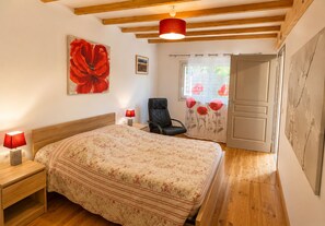 A bedroom with a bed, a chair, a nightstand, a lamp, a painting, and a door leading to another room. - Le Marronnier Vacation Rental – Accessible to People with Disabilities – Mont Ventoux & Cycling (Monieux)