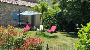 Ein Gebäude aus Stein mit einem Ziegeldach, einer überdachten Terrasse mit roten Liegestühlen und einem Rasen mit Zaun.
