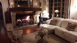A cozy living room with a fireplace, a white leather sofa, a glass coffee table, and a patterned armchair.