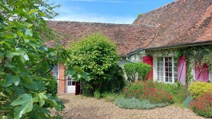 A traditional building with a brick facade, red shutters, and a garden with various plants and flowers.