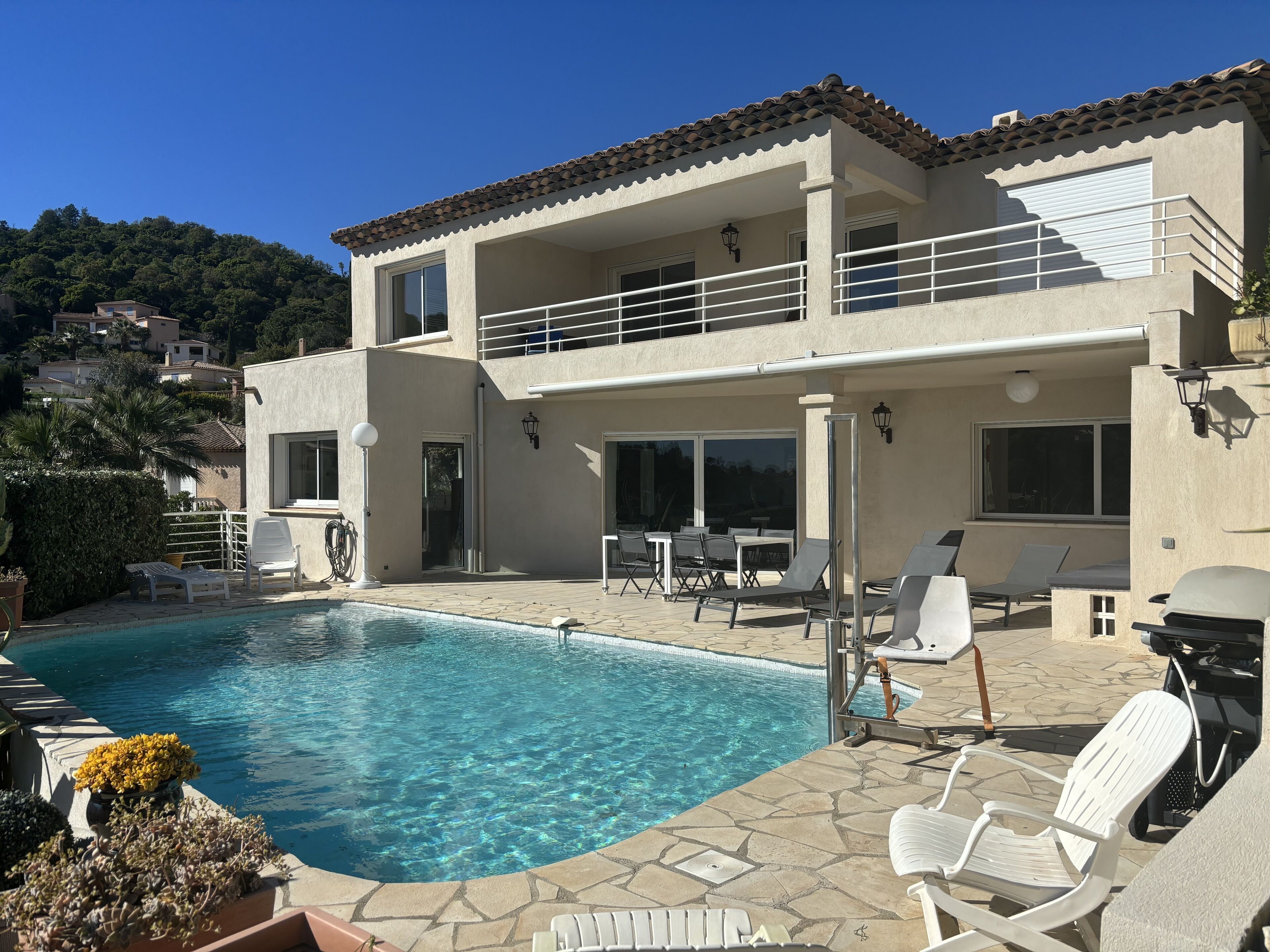A two-story house with a swimming pool, outdoor seating, and a view of the surrounding hills.