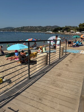 A beach with people sunbathing and swimming, a wooden boardwalk, and a view of the sea and hills in the background. - Stunning ocean view in Les Issambres, pool, air conditioning, pétanque court, wheelchair accessible... (Roquebrune-sur-Argens)