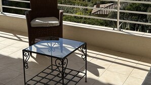A balcony with a wicker chair and a glass table, overlooking a scenic landscape with hills and a body of water. - Stunning ocean view in Les Issambres, pool, air conditioning, pétanque court, wheelchair accessible... (Roquebrune-sur-Argens)