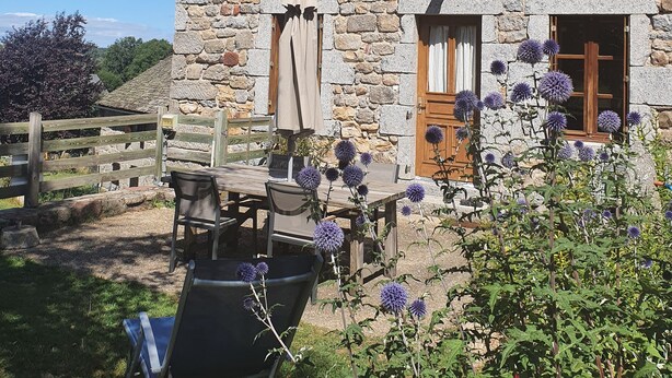 Un bâtiment en pierre avec un toit en tuiles, des volets en bois et une antenne parabolique.
