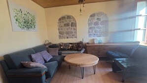Un salon avec un plafond en bois, une table basse ronde, un canapé et un mur en pierre.