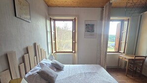 Une chambre avec un plancher en bois, un lit avec une literie blanche, une table de chevet avec une lampe et une fenêtre avec des rideaux.