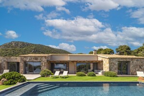 A modern villa with a swimming pool, stone exterior, and a view of a mountain.