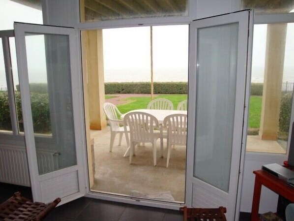 A room with a sliding glass door leading to an outdoor patio with a table and chairs. - Grandcamp-maisy sea view apartment, direct beach access, 4 rooms, sleeps 6 (Grandcamp-Maisy)