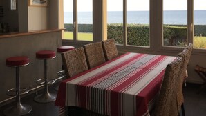 A dining area with a table and chairs, a hanging light fixture, and large windows with a view of the sea. - Grandcamp-maisy sea view apartment, direct beach access, 4 rooms, sleeps 6 (Grandcamp-Maisy)