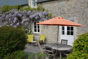 A stone building with a wooden deck, a table, and two yellow chairs. - Stone cottage near Bayeux and D-Day sites, green and quiet. (Crouay)