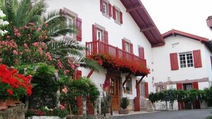 A traditional chalet-style building with a sloped roof, red wooden shutters, and a balcony with red flowers.