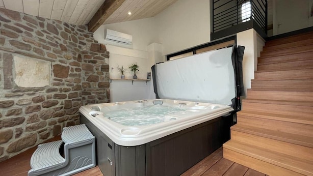 A hot tub in a stone-walled room with wooden flooring and a staircase.