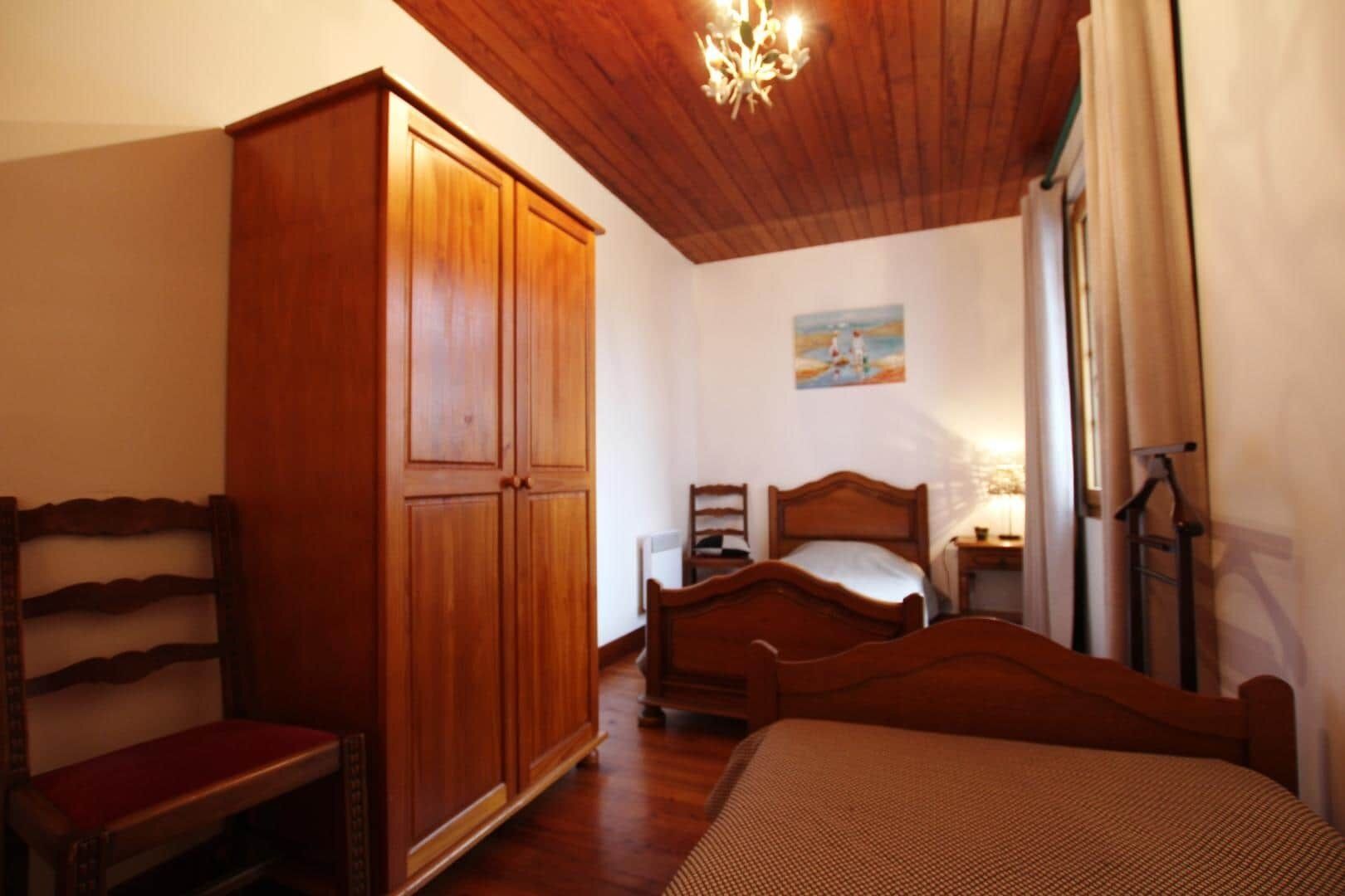 Un dormitorio con un armario de madera, una cama con cabecero de madera, una silla, una mesita de noche con una lámpara y un cuadro en la pared.