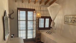 A bedroom with a bed, a desk, a chair, a window with blinds, a hanging lamp, and a wall-mounted air conditioner. - Village house with large rooftop terrace near the beach (Maro - Nerja)
