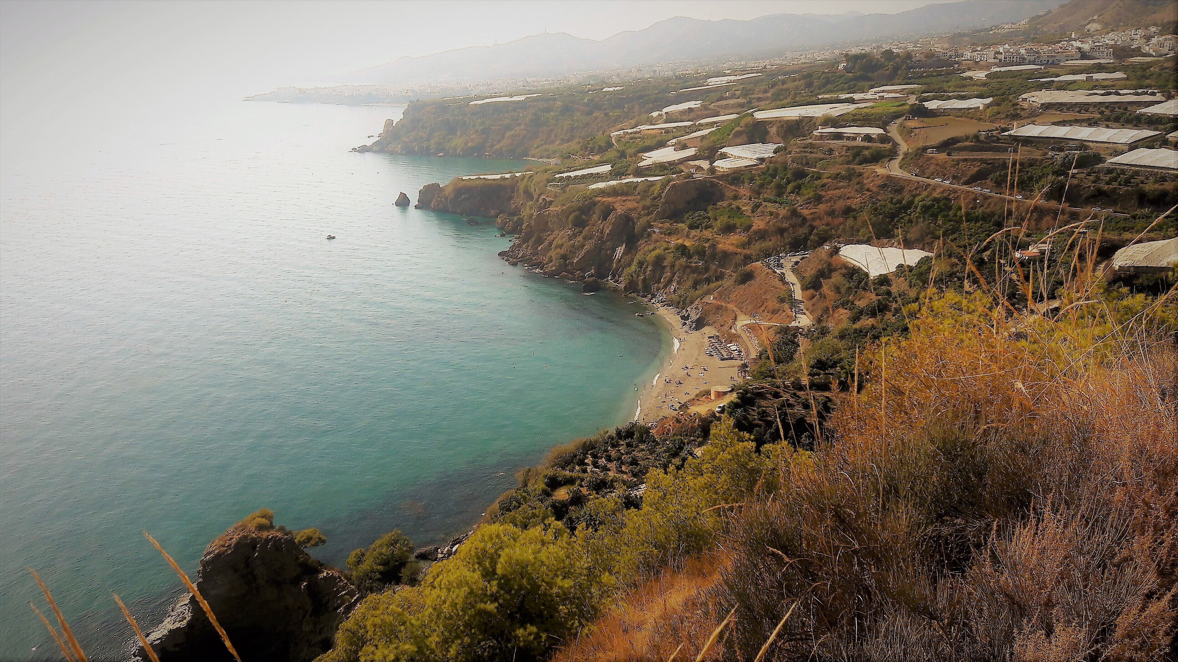 Un paysage côtier avec une plage, des falaises rocheuses et une ville en arrière-plan.