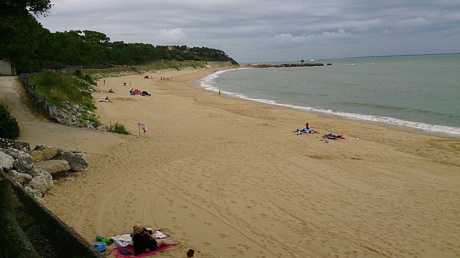Una playa con un muro de piedra, algunas personas y una bandera.