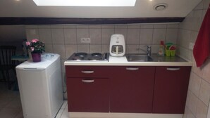 A compact kitchen with a built-in stove, a coffee maker, and a sink. There is a washing machine and a chair visible in the background. - 4-person apartment (Docelles)